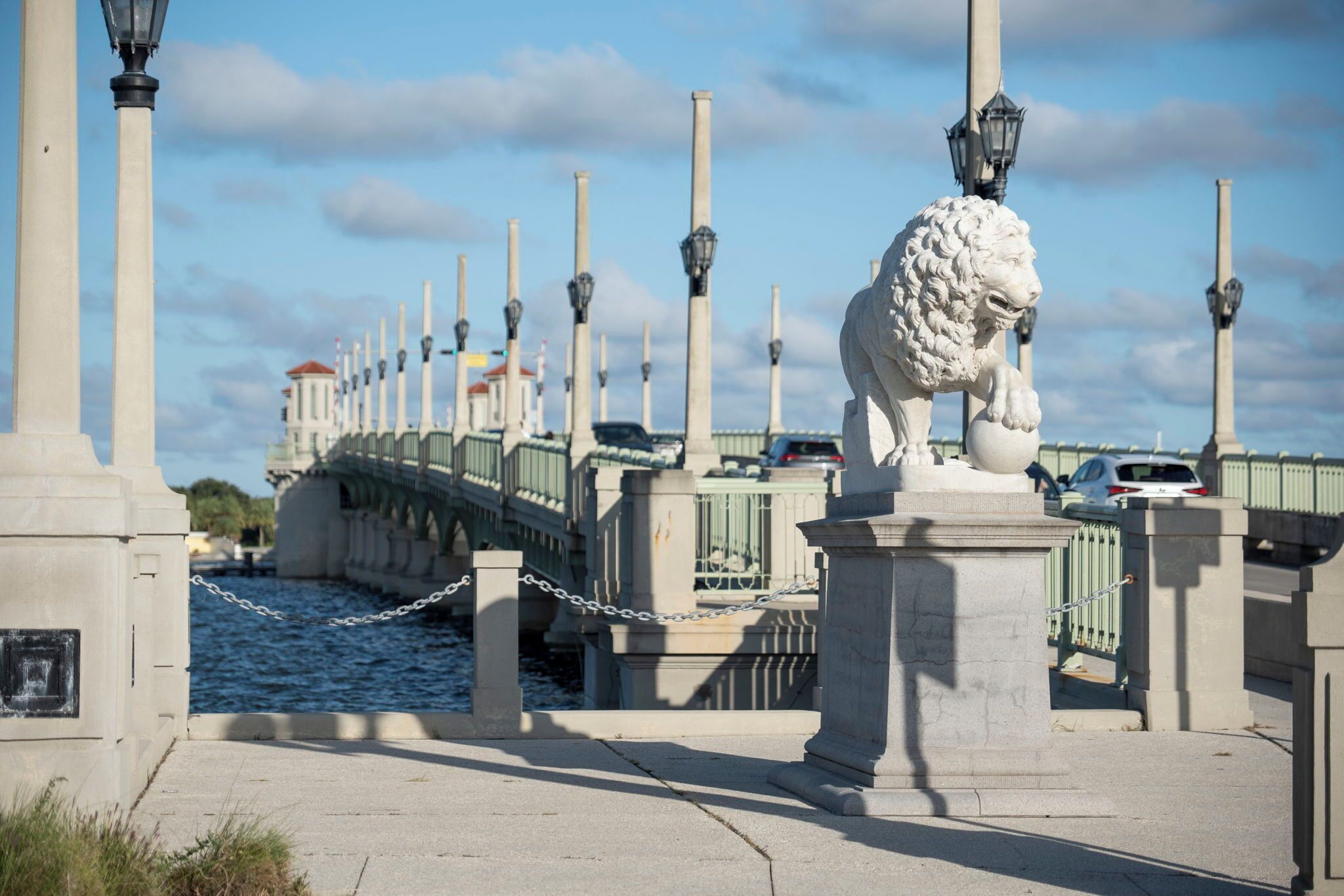 A bridge with a lion statue, chain-link fence, and lamp posts.
