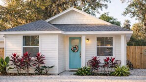 A single-story house with a front porch, a turquoise door, and a wreath. - Encanto Cottage · 3BR · 2 King Beds · 1 mi Historic Downtown · Walk to Marina (St. Augustine)