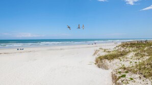 Une plage avec une promenade en bois, un ciel dégagé et des vagues.
