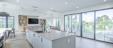 A modern kitchen with a large island, a dining area, and a balcony with a view.