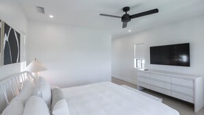 Un dormitorio moderno con cama, ventilador de techo, televisor y cómoda.