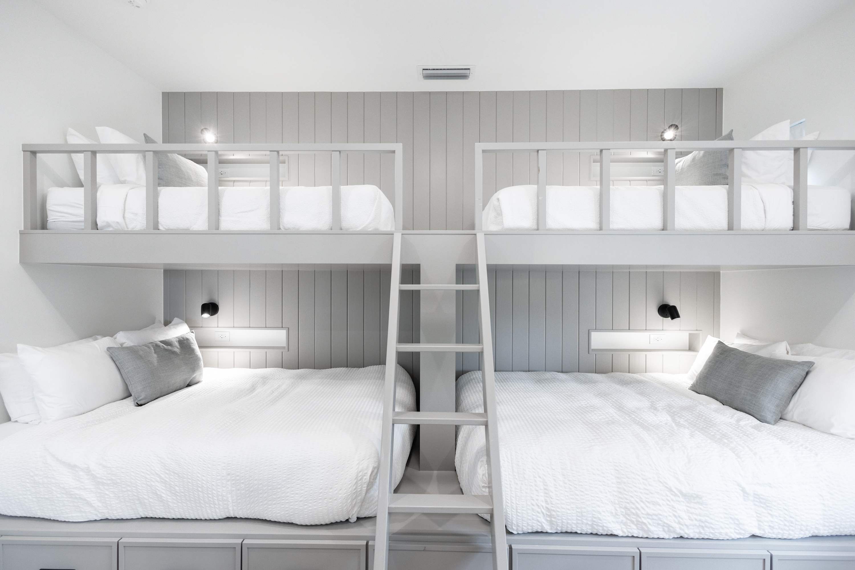 Een slaapkamer met een stapelbed, twee bedden, elk met kussens en een nachtkastje.