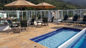 A poolside area with lounge chairs and umbrellas, a clear view of the surrounding hills, and a pool with blue tiles. - RESIDENCIAL VISTA VERDE (Ubatuba)