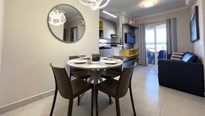 A modern living room with a round dining table, dark chairs, a large mirror, and a contemporary light fixture. - RESIDENCIAL VISTA VERDE (Ubatuba)