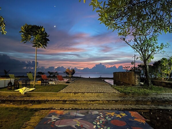 Un sendero pavimentado que conduce a una playa con sillas y una escultura decorativa.