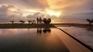 Vista do pôr do sol de uma localização à beira-mar, com uma escultura em formato de coração e calçada molhada refletindo o céu.