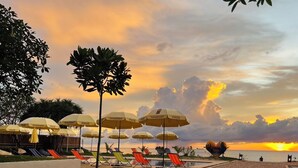 Uma área à beira da piscina com guarda-sóis e espreguiçadeiras, um caminho e vista para o pôr do sol.