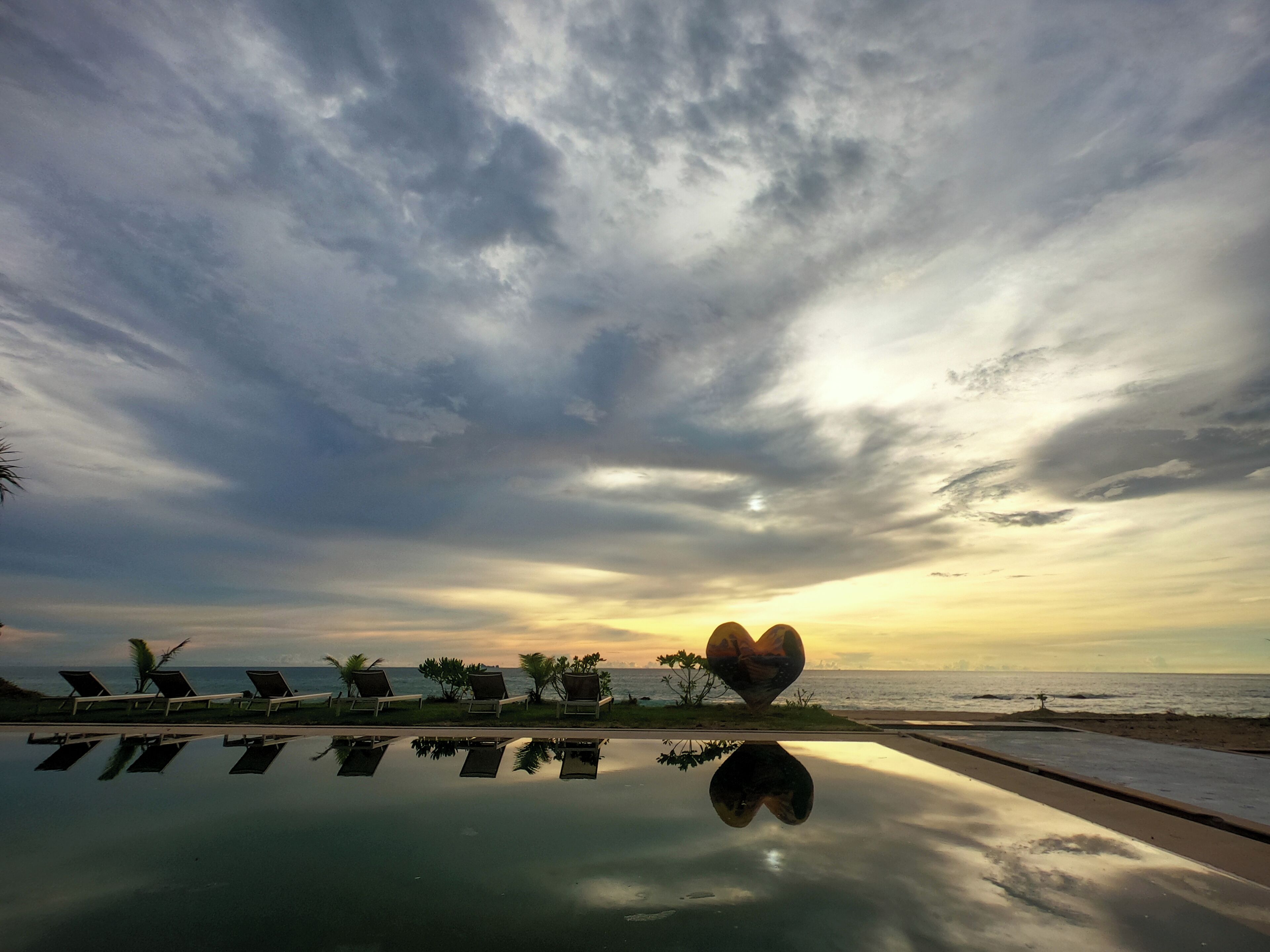 A poolside area with lounge chairs and a heart-shaped decoration, reflecting in the water.