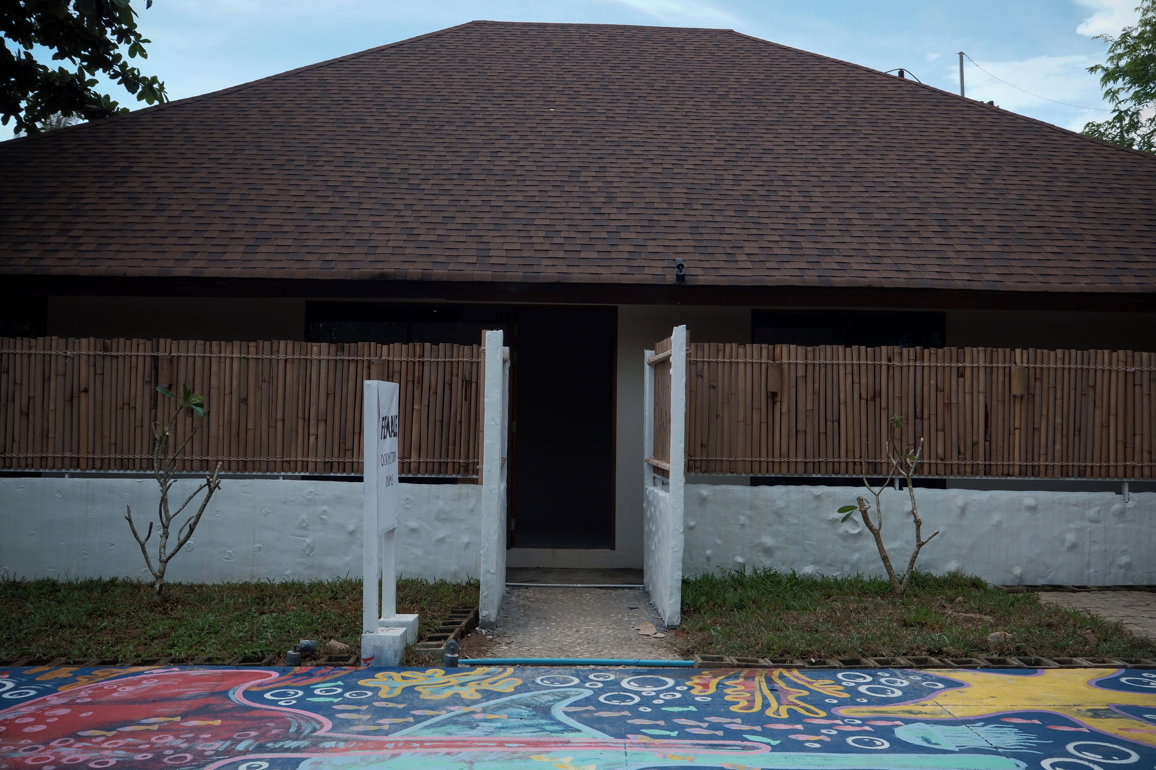 Un edificio con tetto in tegole, recinzione in legno e un motivo decorativo colorato a terra.