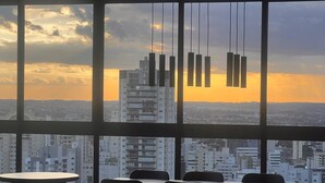 A modern dining area with large windows offering a city view at sunset.