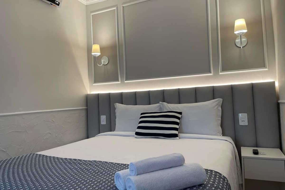 Una cama bien hecha con un edredón estampado, dos almohadas y toallas dobladas.