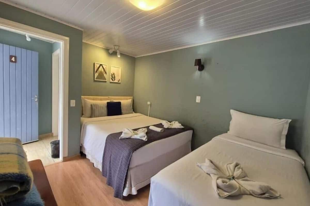 Habitación de hotel con dos camas, suelo de madera, una puerta y una pared con lámpara.