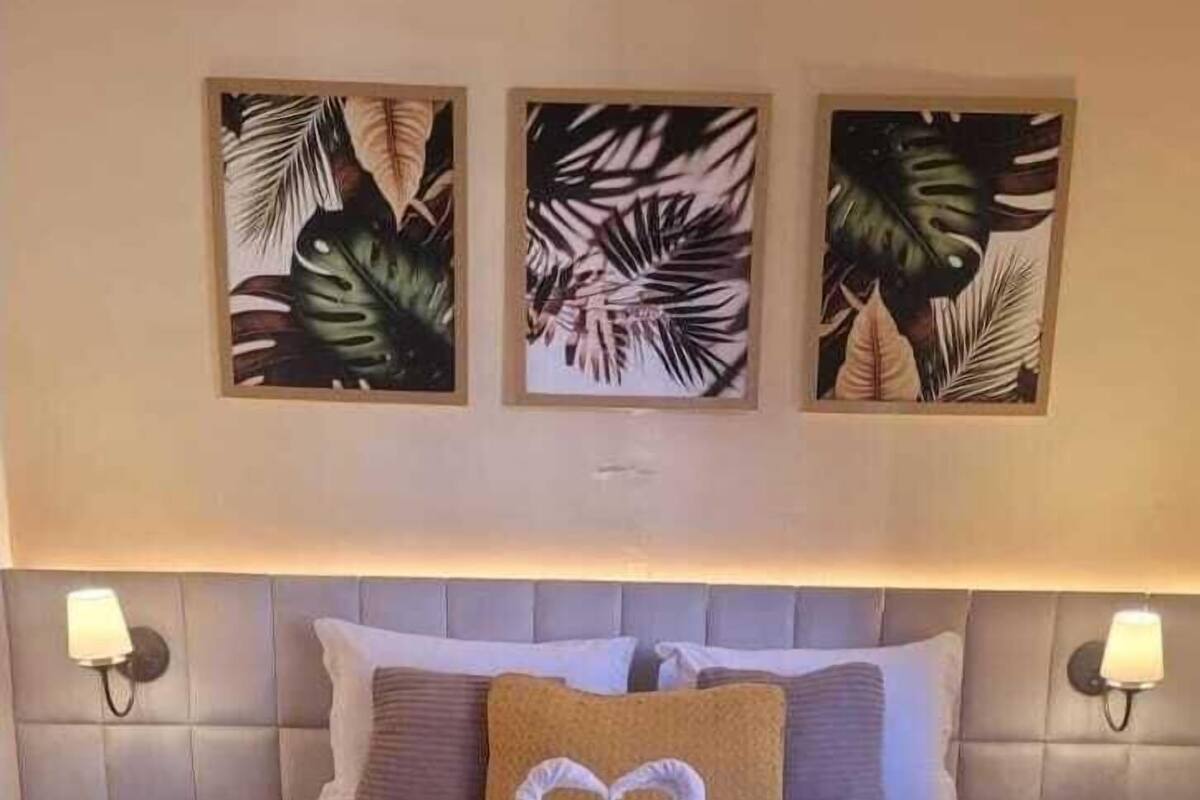 Habitación de hotel con una cama, dos mesitas de noche y tres cuadros con hojas tropicales en la pared.
