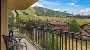 Un balcón con mesa y sillas, con vistas a un barrio residencial con casas y un paisaje montañoso.