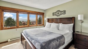 Un dormitorio con una cama grande, cabecero de madera y vistas amplias a través de ventanas grandes.