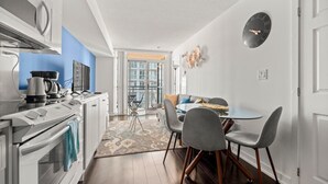 A modern kitchen with a stove, microwave, and coffee maker, a dining area with a table and chairs, and a large window with a view of buildings.