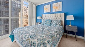 A bedroom with a large bed, two nightstands, a tufted headboard, and two wall-mounted flower paintings.
