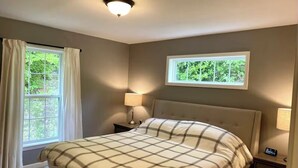 Un dormitorio con una cama, dos mesitas de noche, una ventana con cortinas, una lámpara de techo y vistas a zonas verdes.
