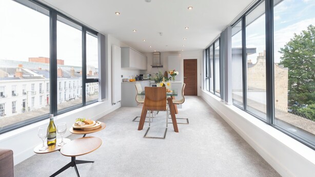 A modern kitchen with large windows, a dining area with a table and chairs, and a view of the cityscape. - Elliot Oliver - The Penthouse 2 Bedroom Apartment With Parking (Cheltenham)