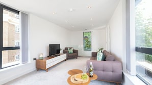 A modern living room with a sofa, TV, and a dining area with a table and chairs. - Elliot Oliver - The Penthouse 2 Bedroom Apartment With Parking (Cheltenham)
