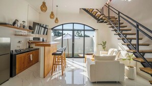 A modern kitchen with a bar area, a dining space with a white sofa, and a staircase leading to an upper level. - Modern Villa with Gym and rare Jungle view in Canggu (Tibubeneng)