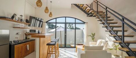 Une cuisine moderne avec un coin bar, un espace repas doté d’un canapé blanc et un escalier menant à un niveau supérieur.