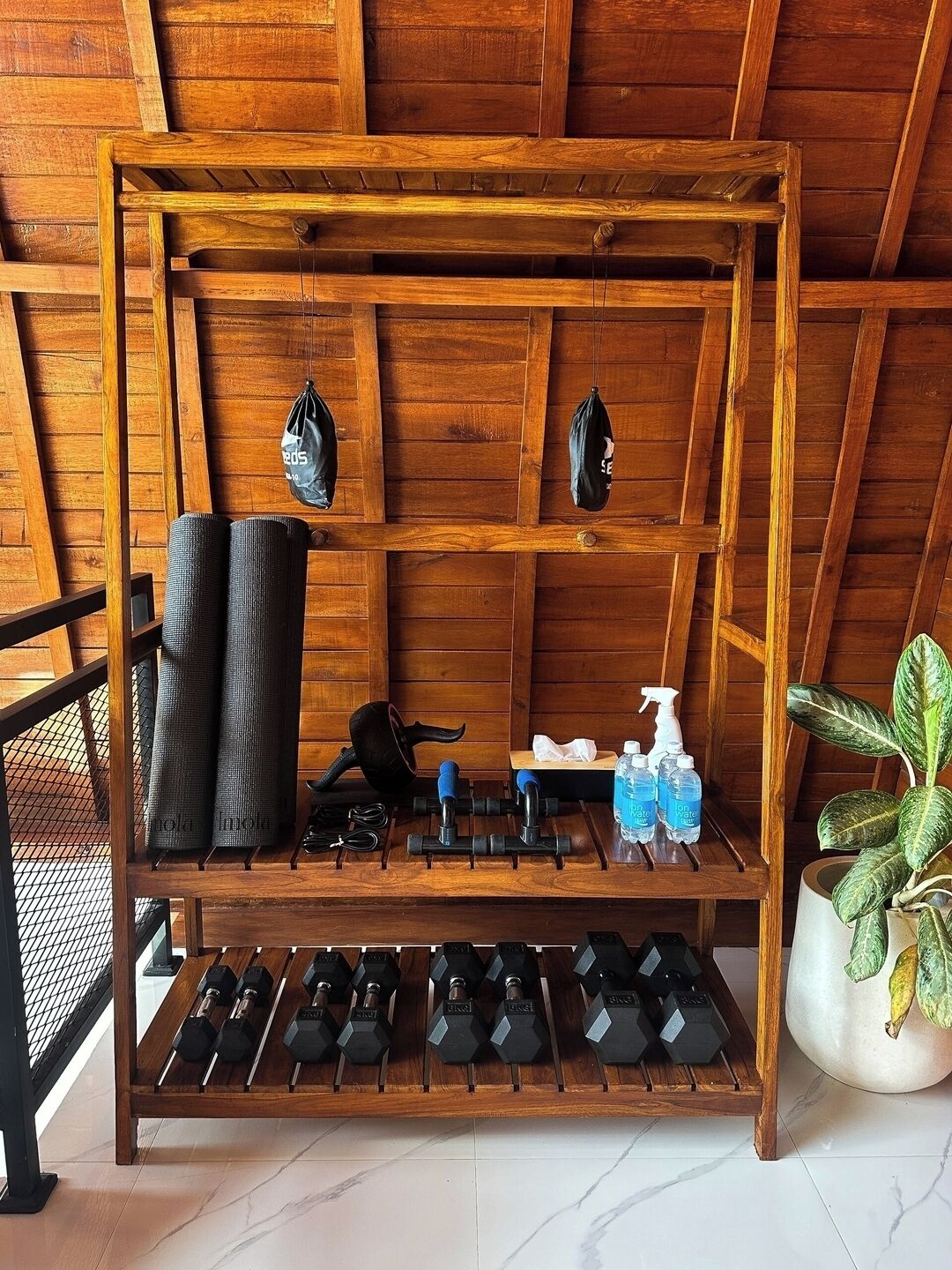 A wooden shelf with yoga mats, dumbbells, and water bottles.