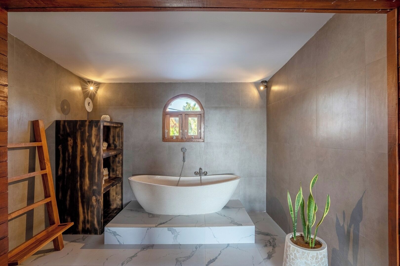 Une salle de bain avec une baignoire sur pieds, une échelle en bois, une étagère avec des objets décoratifs et une plante en pot.