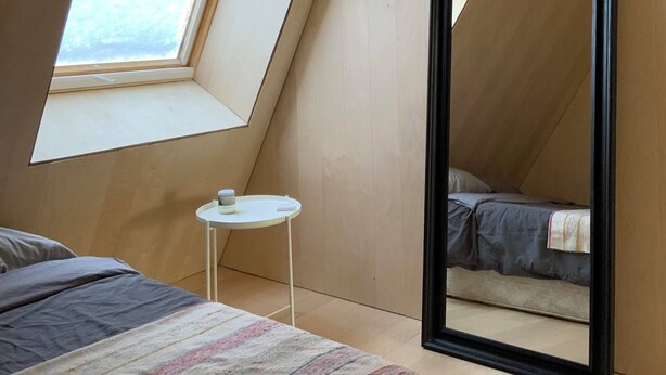 A bedroom with a sloped ceiling, a skylight, a large mirror, a small round table, and a bed with a striped blanket. - Chalet des Sentiers - An architectural experience at Lac Fidèle, Entrelacs  (Entrelacs)