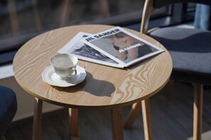 Ein runder Holztisch mit Untertasse und Tasse, und eine Zeitschrift mit dem Titel 'JIL SANDER' darauf.