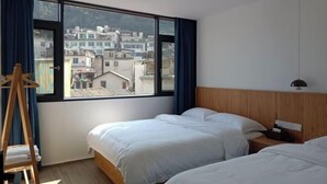 Ein Hotelzimmer mit zwei Betten, einem Holzkopfende, einem Nachttisch und einem großen Fenster mit Blick auf Gebäude.