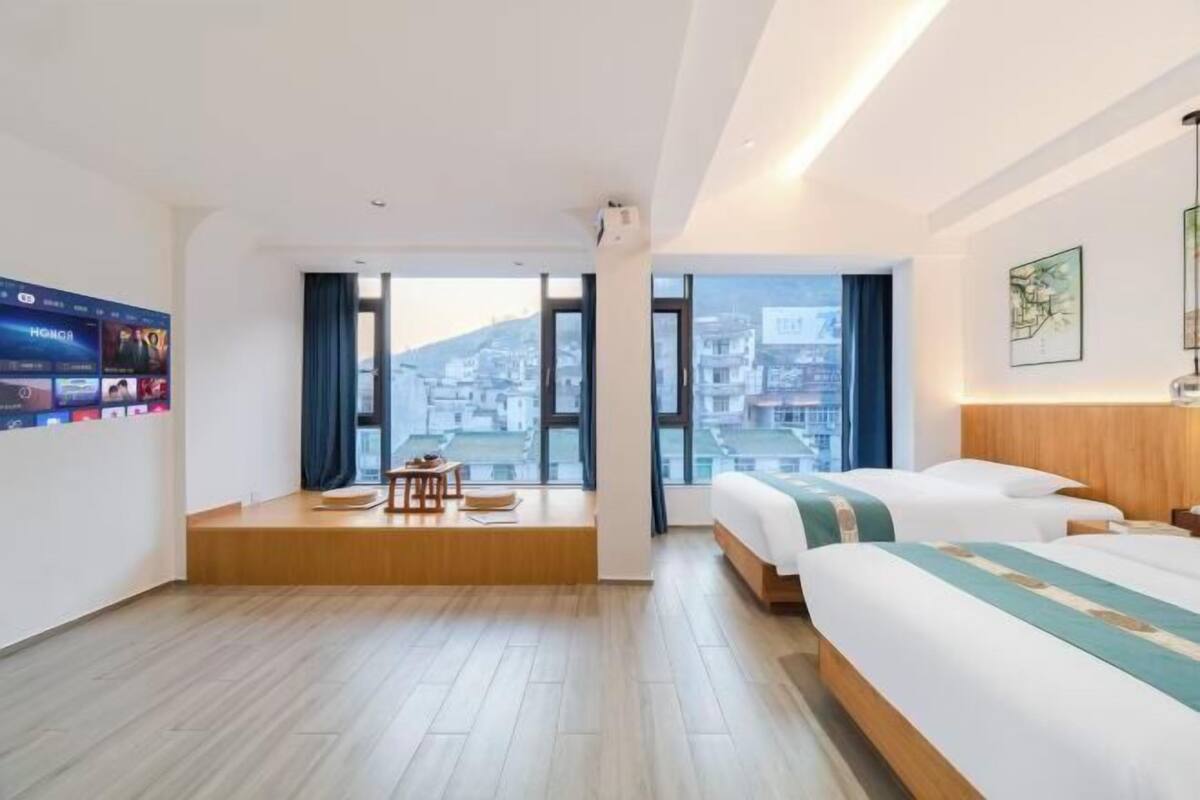 Une chambre d’hôtel avec une grande fenêtre, un lit, un bureau et un téléviseur à écran plat.