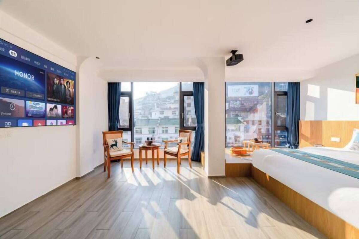 Une chambre d’hôtel dotée d’une grande fenêtre, d’un lit, d’un téléviseur fixé au mur et d’un coin salon avec des fauteuils.