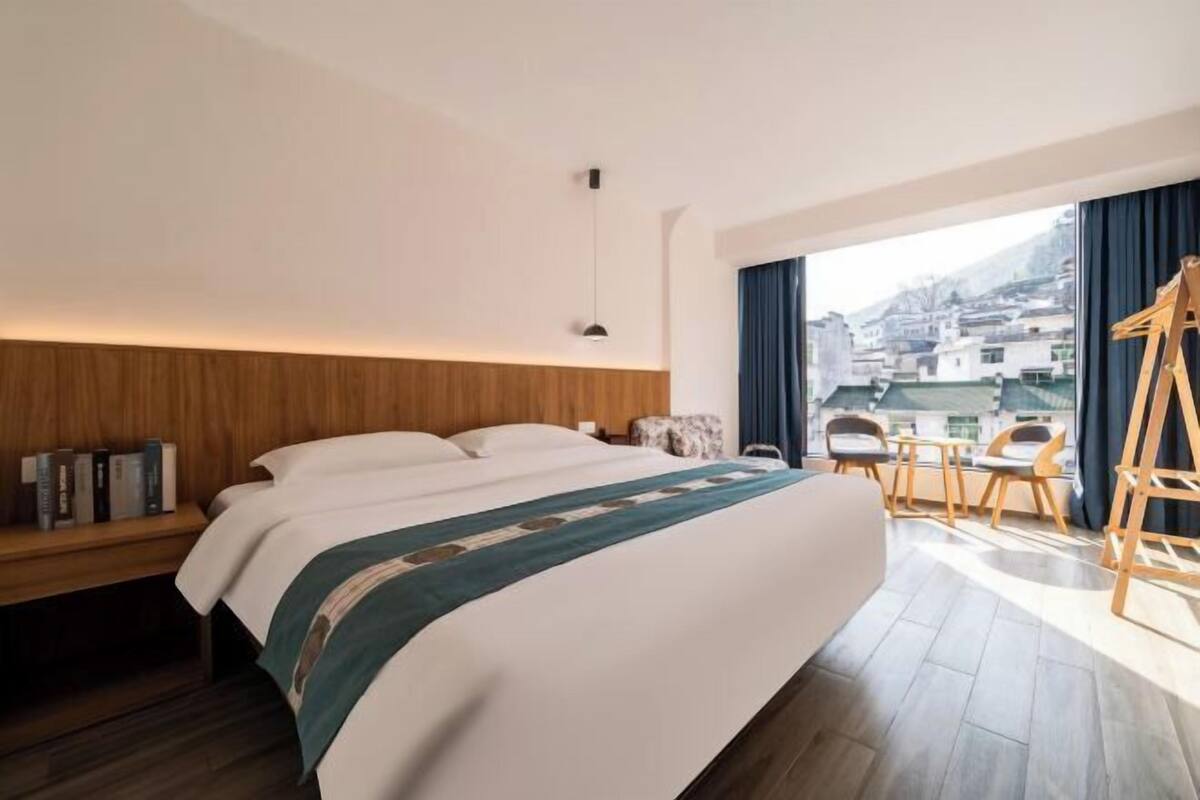 Une chambre d’hôtel avec un lit, un bureau, une chaise, une échelle et une vue sur les bâtiments par la fenêtre.