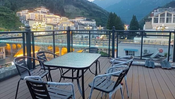 Eine Terrasse mit Tisch und Stühlen mit Blick auf eine gebirgige Landschaft und Gebäude.