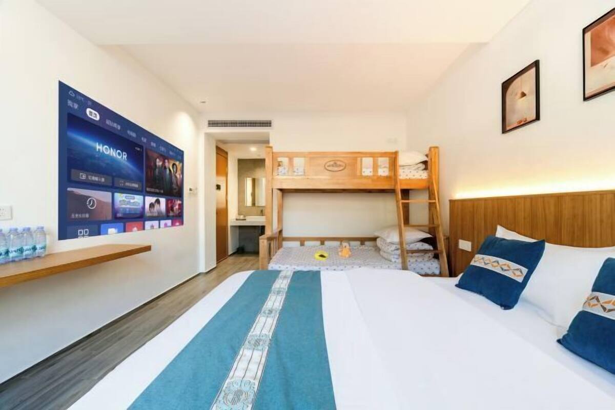 Une chambre d’hôtel avec un lit superposé, une grande télévision à écran plat, une tête de lit en bois et une couvre-lit bleue à motifs.