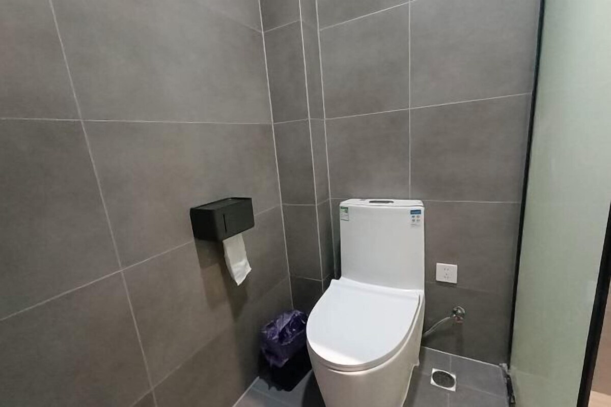 Un baño pequeño y moderno con inodoro, un cubo de basura y dispensador de papel en la pared.