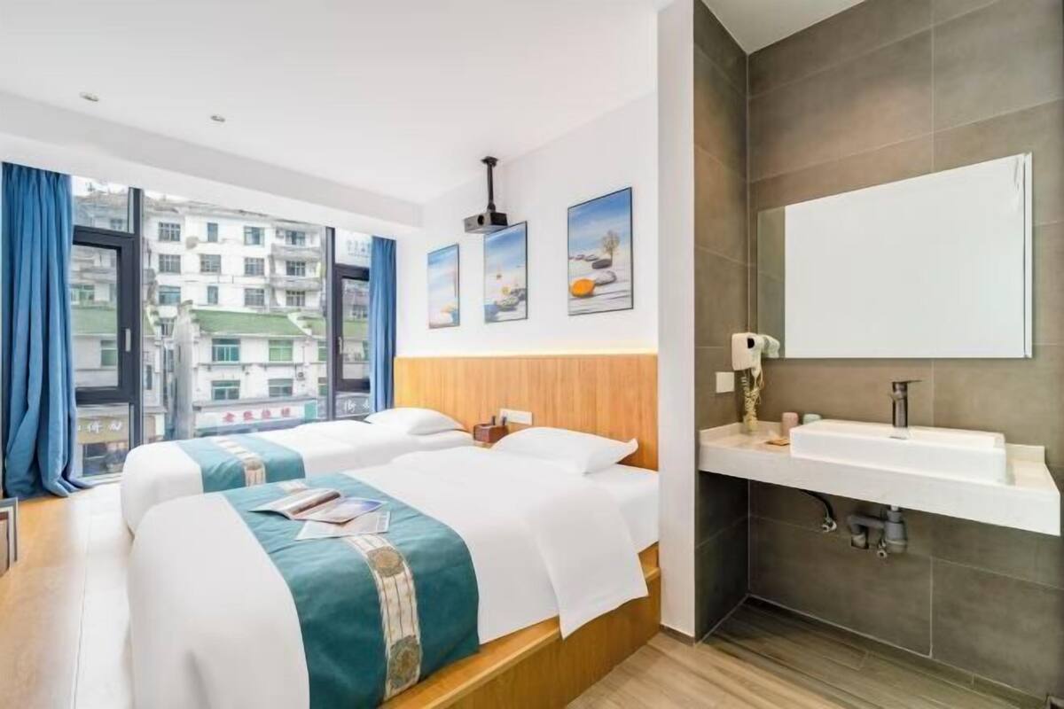Une chambre d’hôtel avec deux lits, une grande fenêtre, une salle de bain avec un lavabo et des œuvres d’art accrochées aux murs.
