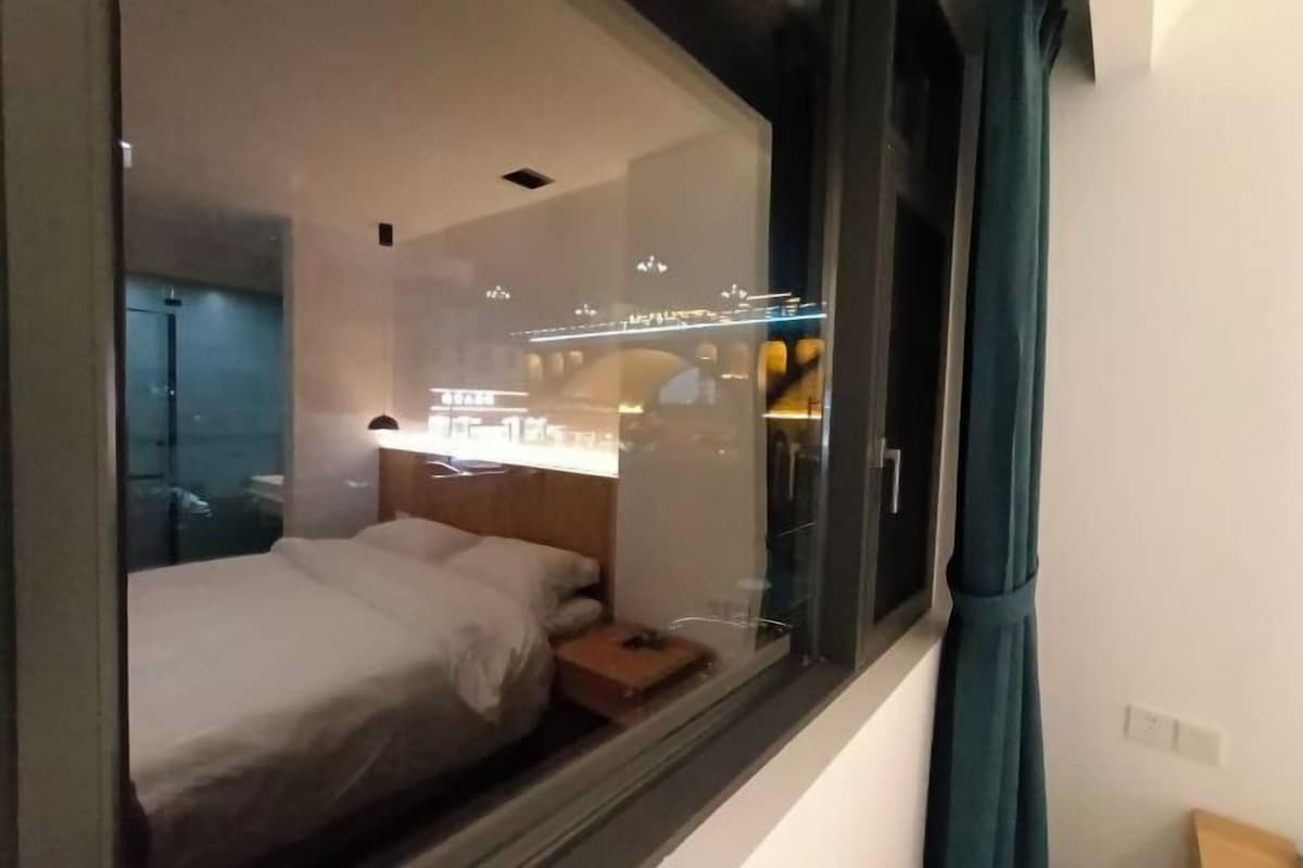 Habitación de hotel moderna con una cama grande, una mesita de noche y una ventana con vistas a la ciudad.