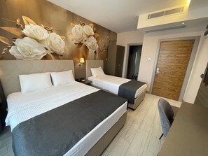 A hotel room with two beds, a wooden door, and a wall with a floral design. - Mithras Hotel (Izmir)