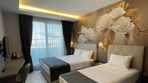 Une chambre d’hôtel avec deux lits, un bureau, une chaise, une lampe et une grande fresque murale représentant des motifs floraux.