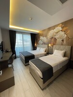 Habitación de hotel con dos camas, un escritorio, una silla, una lámpara y un gran mural floral en la pared.