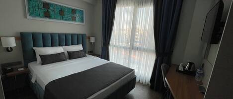 Una habitación de hotel con una cama grande, un escritorio, una silla, un televisor y un cuadro en la pared.