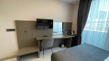 A modern hotel room with a bed, a desk, a chair, a TV, and a window with curtains.