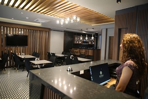 Un moderno bar con una barra alargada, diferentes opciones de asientos y un televisor montado en la pared.