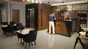 Un espace d’accueil moderne avec un comptoir de réception en bois, un sol à motifs noir et blanc et des chaises noires agrémentées de détails dorés.
