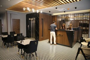 Una moderna zona de recepción con un mostrador de madera, suelo de estampado blanco y negro, y sillas negras con detalles dorados.
