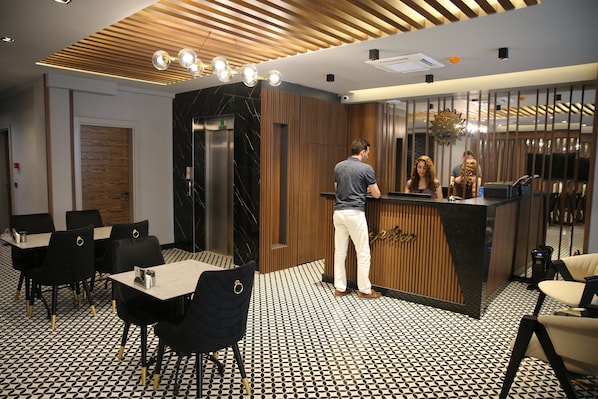 A modern reception area with a wooden reception desk, black and white patterned floor, and black chairs with gold accents. - Mithras Hotel (Izmir)