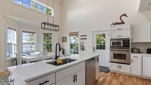 Een moderne keuken met witte kasten, een groot keukeneiland met een spoelbak en uitzicht op de omgeving.
