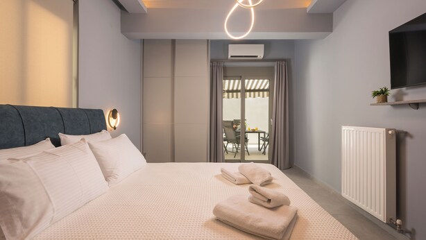 A modern hotel room with a large bed, a flat-screen TV mounted on the wall, and a view of the outdoor patio through a glass door. - Casa Amarillo is the perfect place for your holidays (Chania)